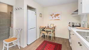 A compact kitchen with a refrigerator, a dining table with chairs, a world map on the wall, and a red patterned rug. - Mountain View Bliss - Albert Town Holiday Unit (Albert Town)
