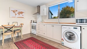 A modern kitchen with a large window, a washing machine, and a dining area with a red rug. - Mountain View Bliss - Albert Town Holiday Unit (Albert Town)