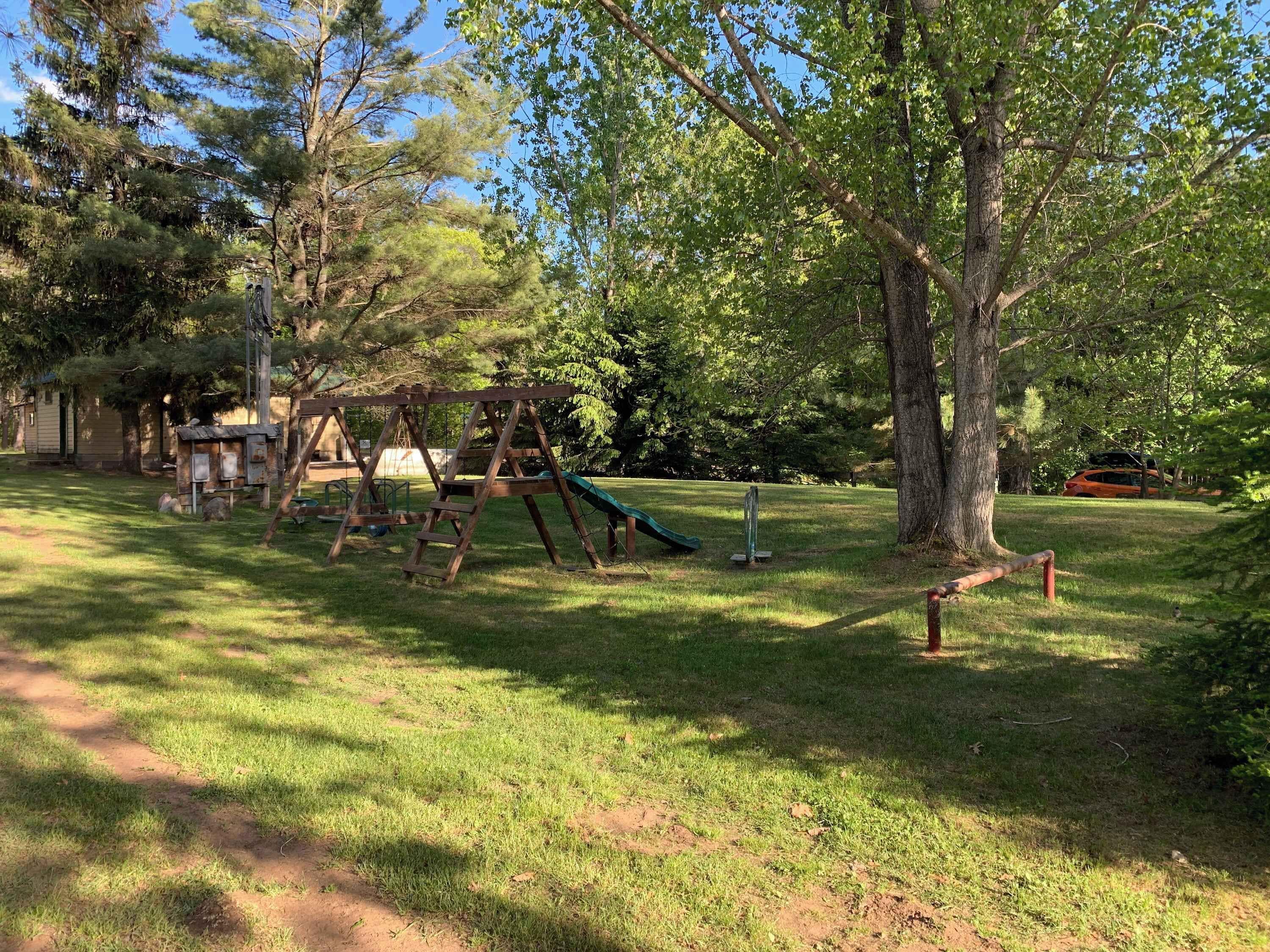 A playground with swings and a slide, surrounded by trees and grass.