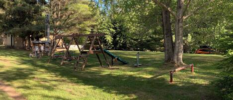 A playground with swings and a slide, surrounded by trees and grass.