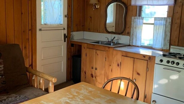 Ett kompakt kök med träskåp, en diskho, en spis och ett matbord med stolar.