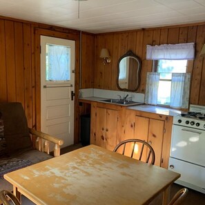 A compact kitchen with wooden cabinets, a sink, a stove, and a dining table with chairs.