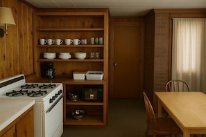 Eine kompakte Küche mit Herd, Backofen und Mikrowelle, Holzböden mit Geschirr, einer Kaffeemaschine und einem Essbereich mit Tisch und Stühlen.