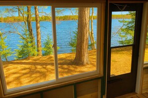 A cabin with a large window overlooking a lake surrounded by trees.