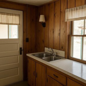 A kitchen with wooden paneling, a double sink, a window with a view, and a door with a window treatment.