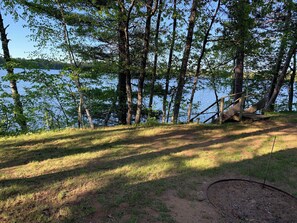 A natural setting with a dirt path leading to a wooden structure near a body of water, surrounded by trees.