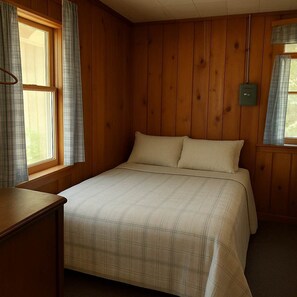 Ein Zimmer mit Holzwänden, einem Bett, einem kleinen Tisch und einem Fenster mit Vorhängen.