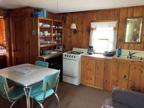 A compact kitchen with wooden cabinets, a stove, a sink, and a dining table with chairs.