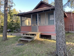 Une cabane avec un porche à l’avant, une porte et une fenêtre.