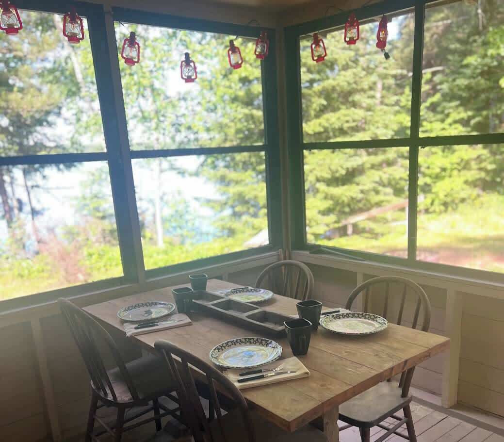 A dining area with a table set for four, surrounded by chairs, large windows with a view of greenery, and red lanterns hanging above.