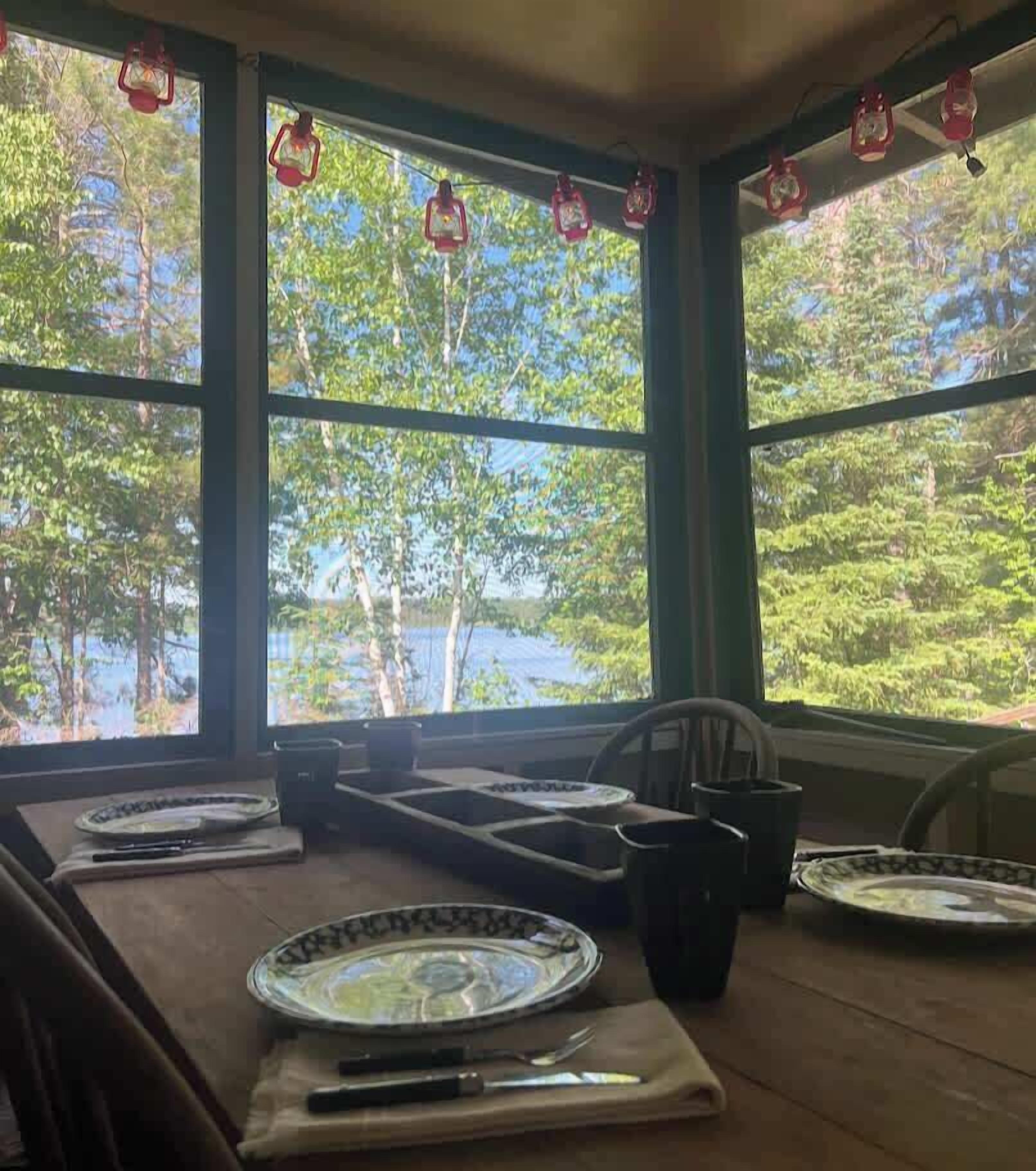 A dining area with a view of a lake and trees, featuring a table set with plates, a knife, and a pitcher.