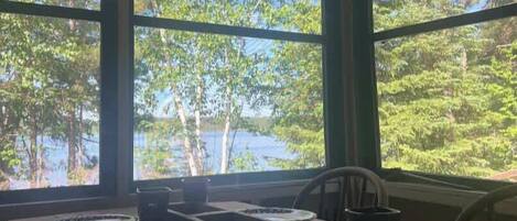 A dining area with a view of a lake and trees, featuring a table set with plates, a knife, and a pitcher.