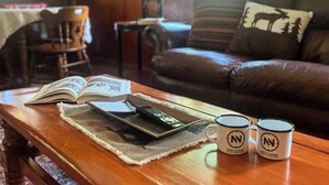 Una sala de estar acogedora con un sofá de cuero, una mesita de centro con libros y tazas, y una lámpara.
