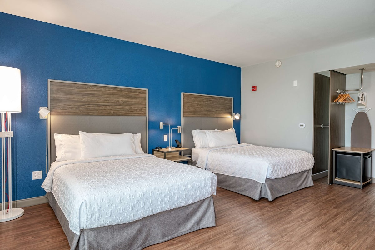 Une chambre d’hôtel avec deux lits, un mur d’accent bleu, un plancher en bois, une table de chevet avec une lampe et une armoire avec un miroir.