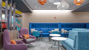 A modern lounge area with blue seating, purple armchairs, and white tables. - Tru By Hilton Indianapolis Lawrence, In (Indianapolis)