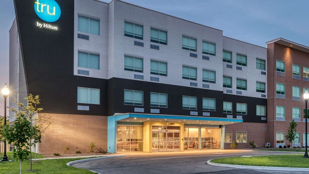 A hotel with a modern design, featuring a prominent 'tru by Hilton' sign, multiple floors, and a well-lit entrance. - Tru By Hilton Indianapolis Lawrence, In (Indianapolis)