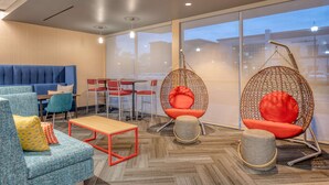 A modern lounge area with a blue sofa, red chairs, a wooden table, and a hanging chair with a red cushion. - Tru By Hilton Indianapolis Lawrence, In (Indianapolis)