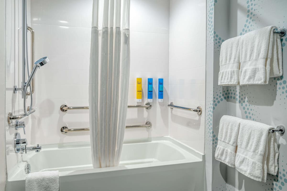 Une salle de bain moderne équipée d’une baignoire, d’une douche et de barres d’appui. On peut voir trois articles de toilette accrochés au mur.