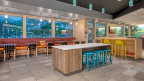 A modern cafe with a wooden bar, red seating, and large windows. - Tru By Hilton Indianapolis Lawrence, In (Indianapolis)