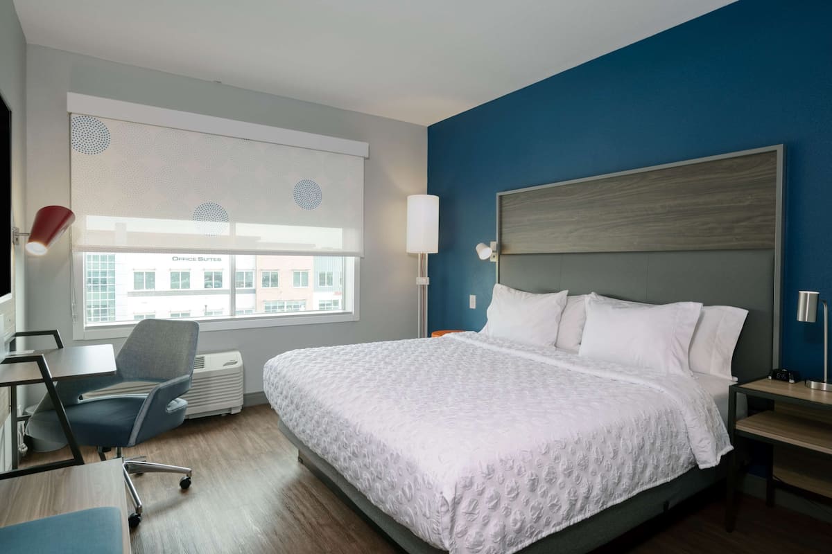 Une chambre d’hôtel avec un grand lit, un bureau, une chaise et une fenêtre avec des stores.