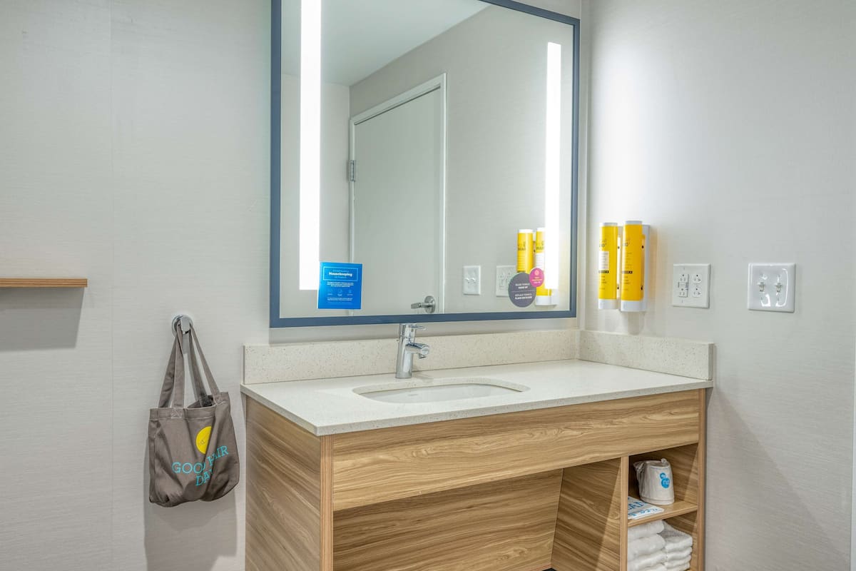Une salle de bain avec un meuble-lavabo en bois, un évier, un miroir et un porte-serviettes.