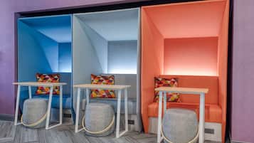A modern room with three seating areas, each with a table and ottoman. The room has a geometric patterned wall and a carpeted floor.
