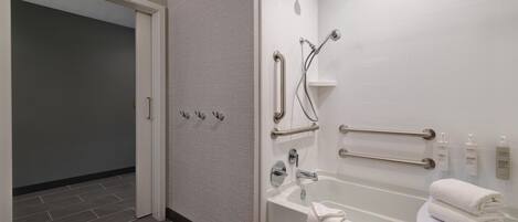 A modern bathroom with a bathtub, grab bars, and a shower head.
