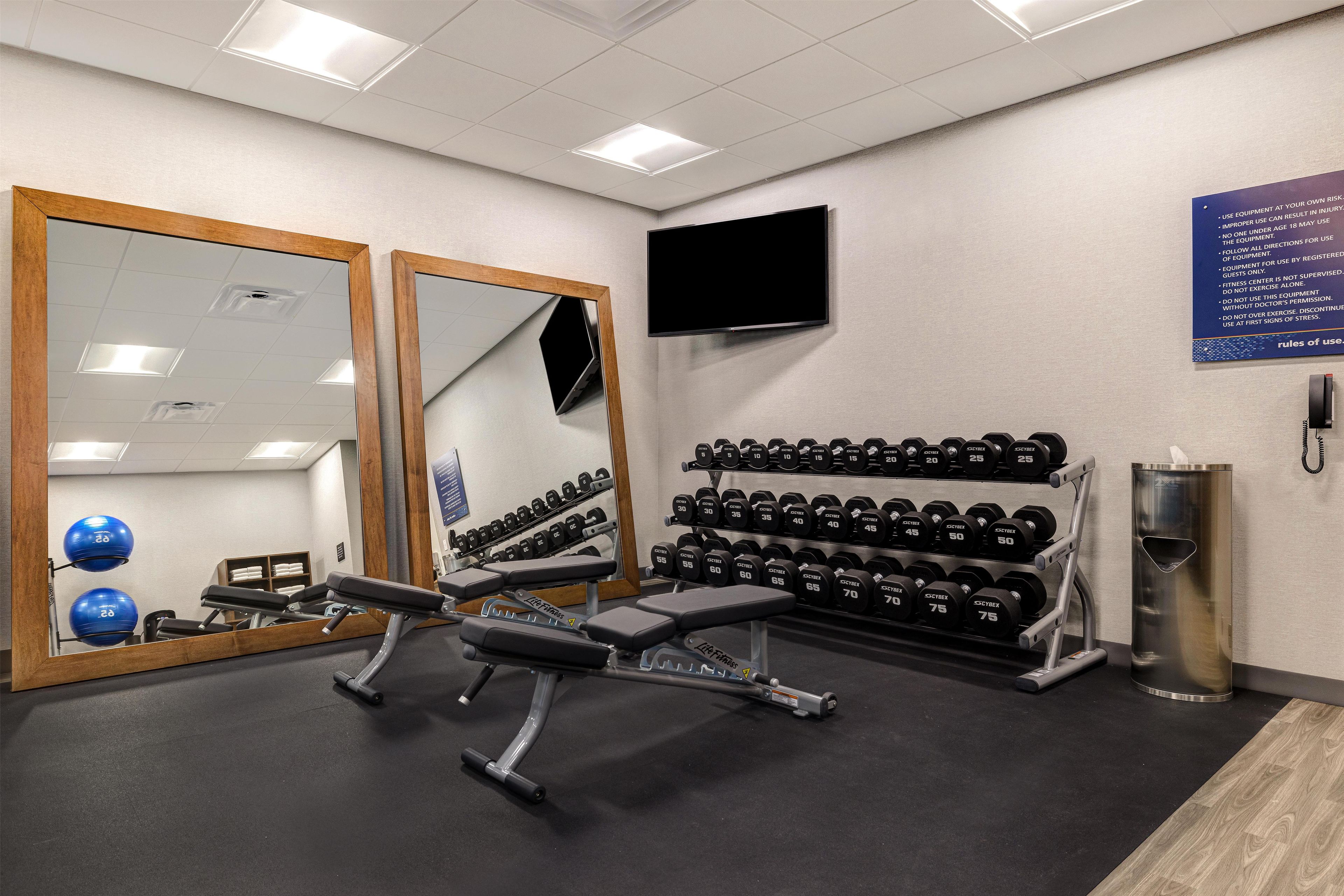 Ein Fitnessraum mit Trainingsgeräten, einem Spiegel, einem Fernseher und einem Schild mit Nutzungsregeln.