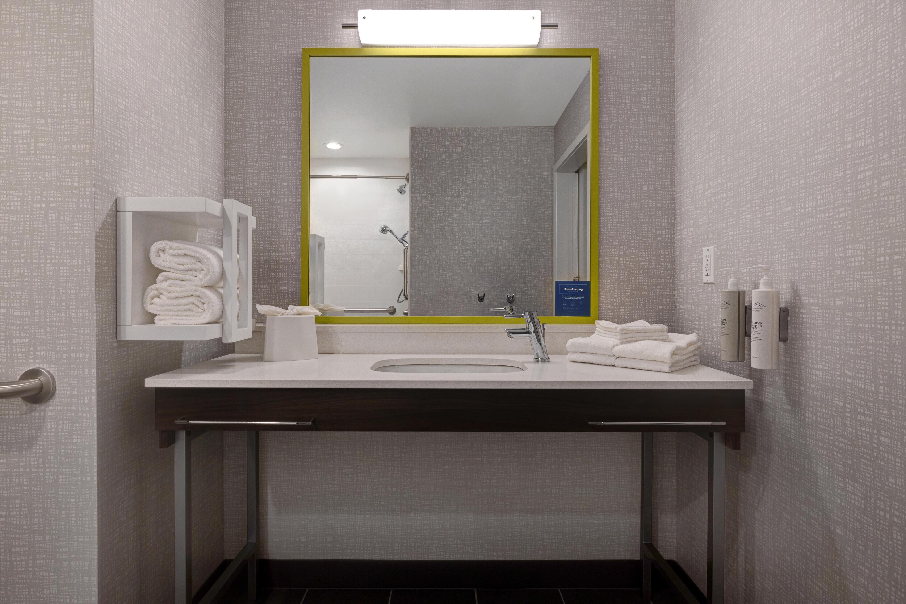 A modern bathroom with a white sink, a mirror with a yellow frame, a towel rack, and a shower area.