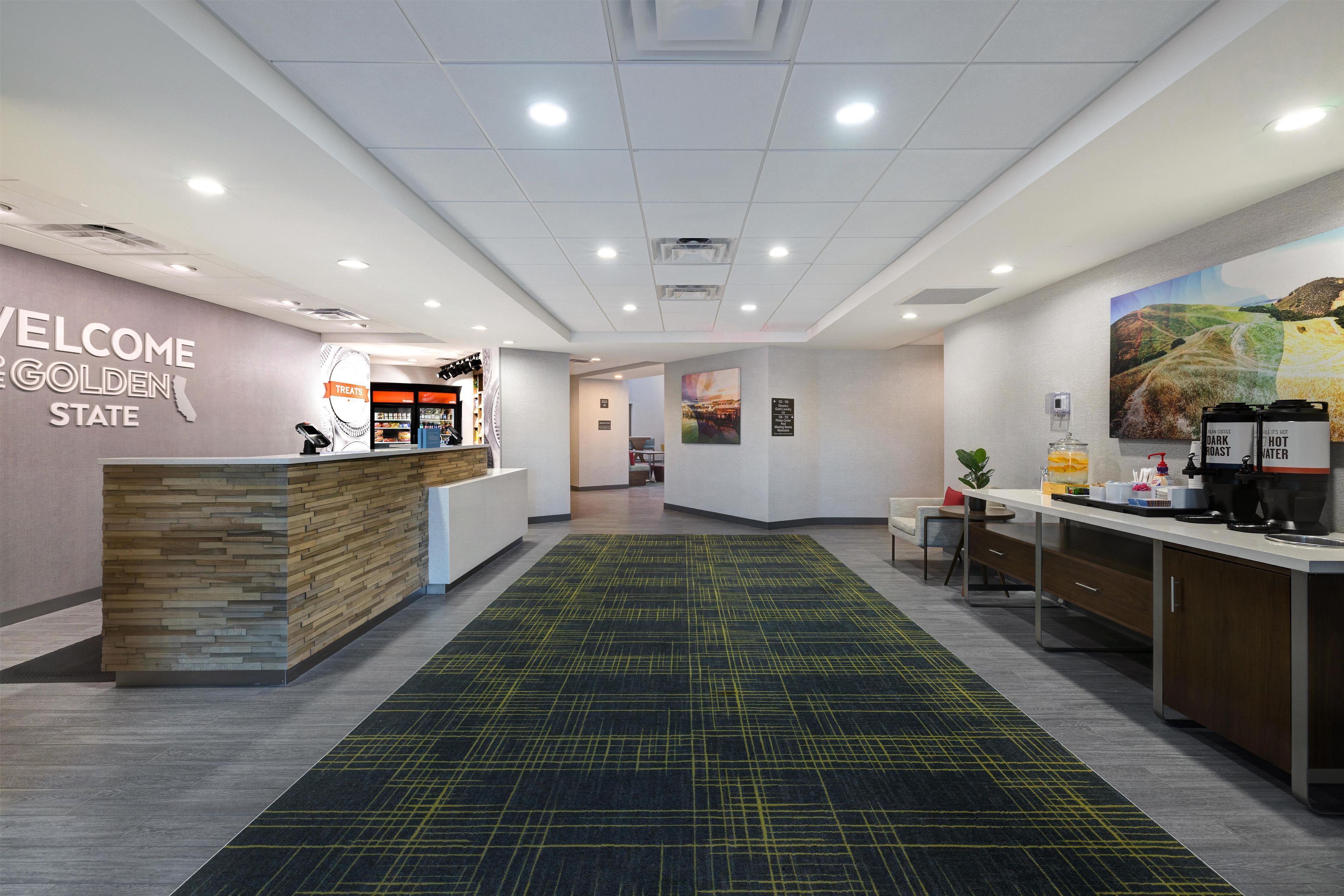 A reception area with a 'Welcome Golden State' sign, a counter with a coffee machine, and a painting on the wall.