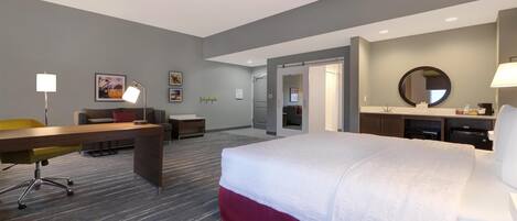 A hotel room with a bed, desk, chair, and a bathroom with a mirror.
