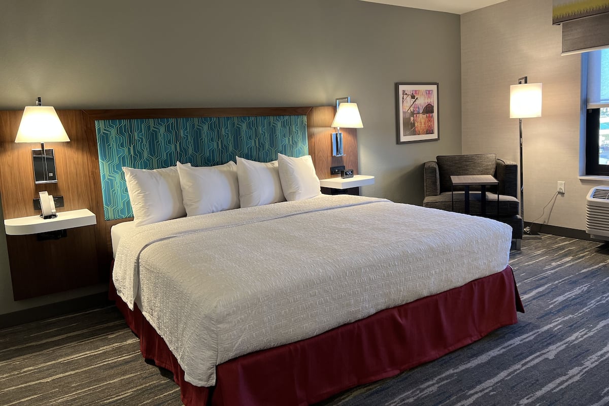 Een hotelkamer met een groot bed, twee bedlampen, een bureau, een stoel en een raam.