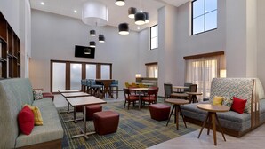 A spacious hotel lobby with a seating area, tables, and a television mounted on the wall. - Hampton Inn & Suites Marina (Marina)