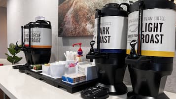 A coffee station with three coffee dispensers labeled "Decaf Roast," "Dark Roast," and "Light Roast." There are also coffee pods, a coffee grinder, and a small plant on the counter.