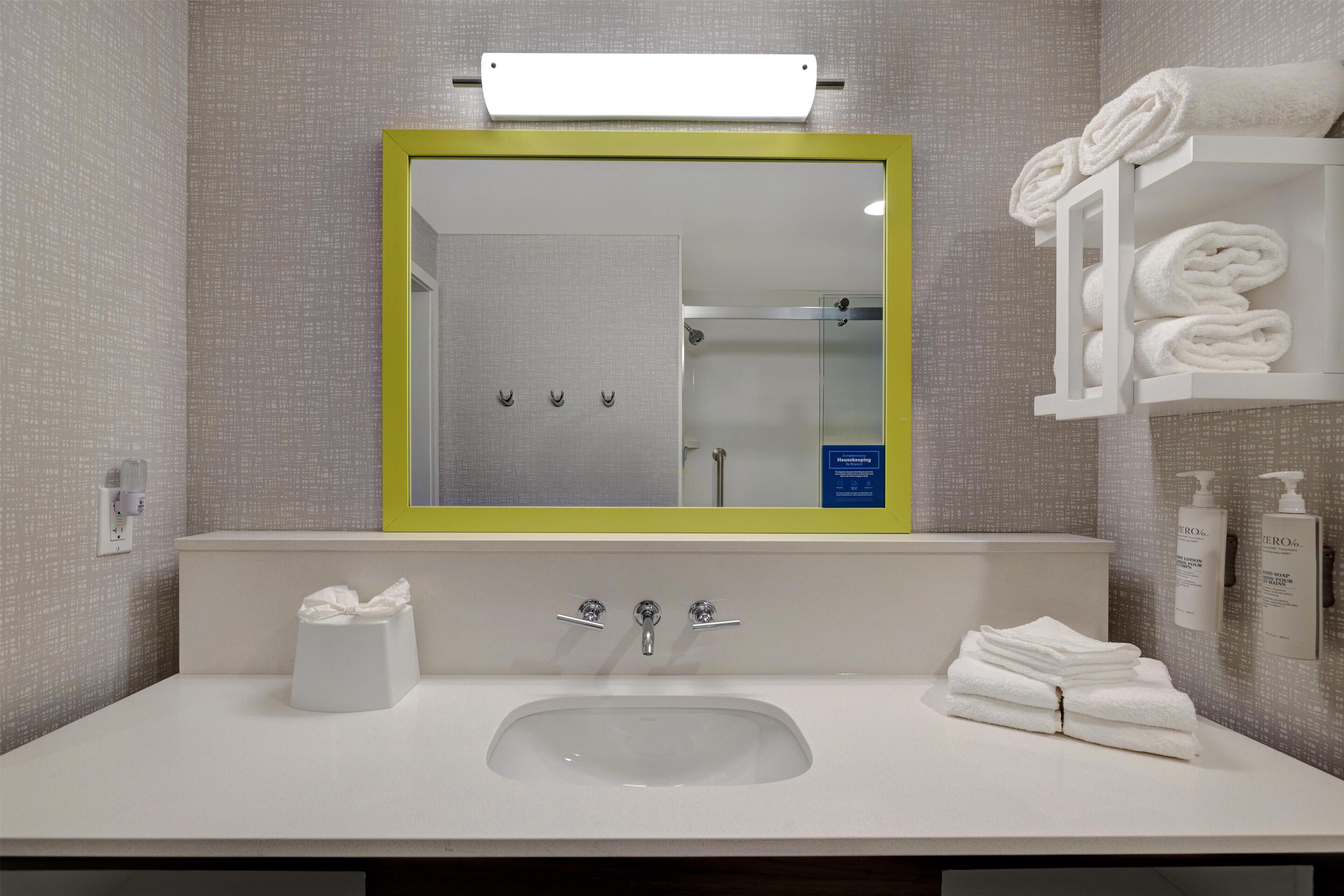 Un baño con un lavamanos blanco, un espejo con marco amarillo y un perchero con toallas dobladas.