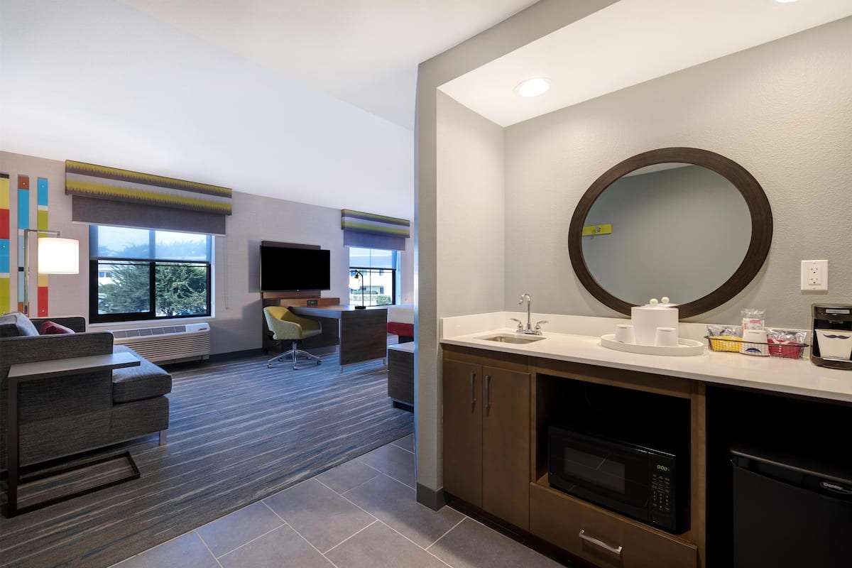Een moderne hotelkamer met een kitchenette, een grote spiegel, een bank en een televisie.