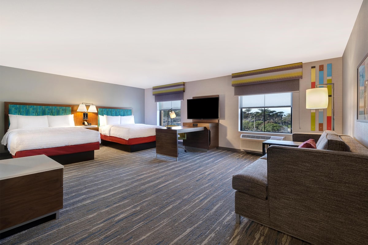 Een hotelkamer met twee bedden, een bureau, een televisie en een groot raam.