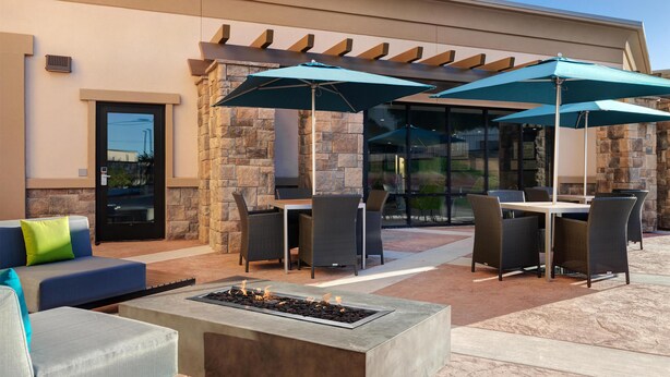 An outdoor patio with stone walls, a fire feature, and outdoor furniture under umbrellas. - Hampton Inn & Suites Marina (Marina)