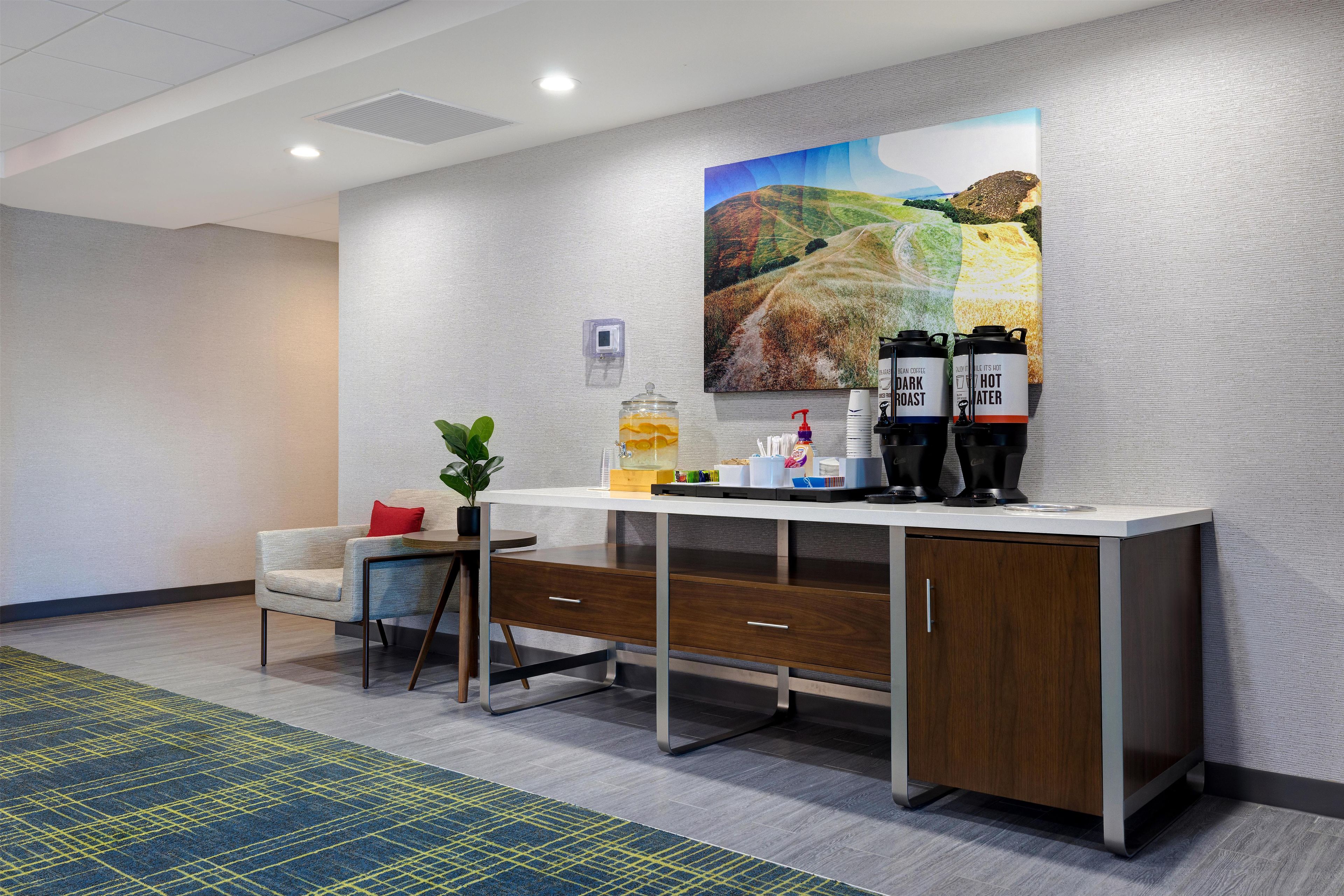 Uma área de recepção de hotel com balcão, máquina de café e um quadro na parede.
