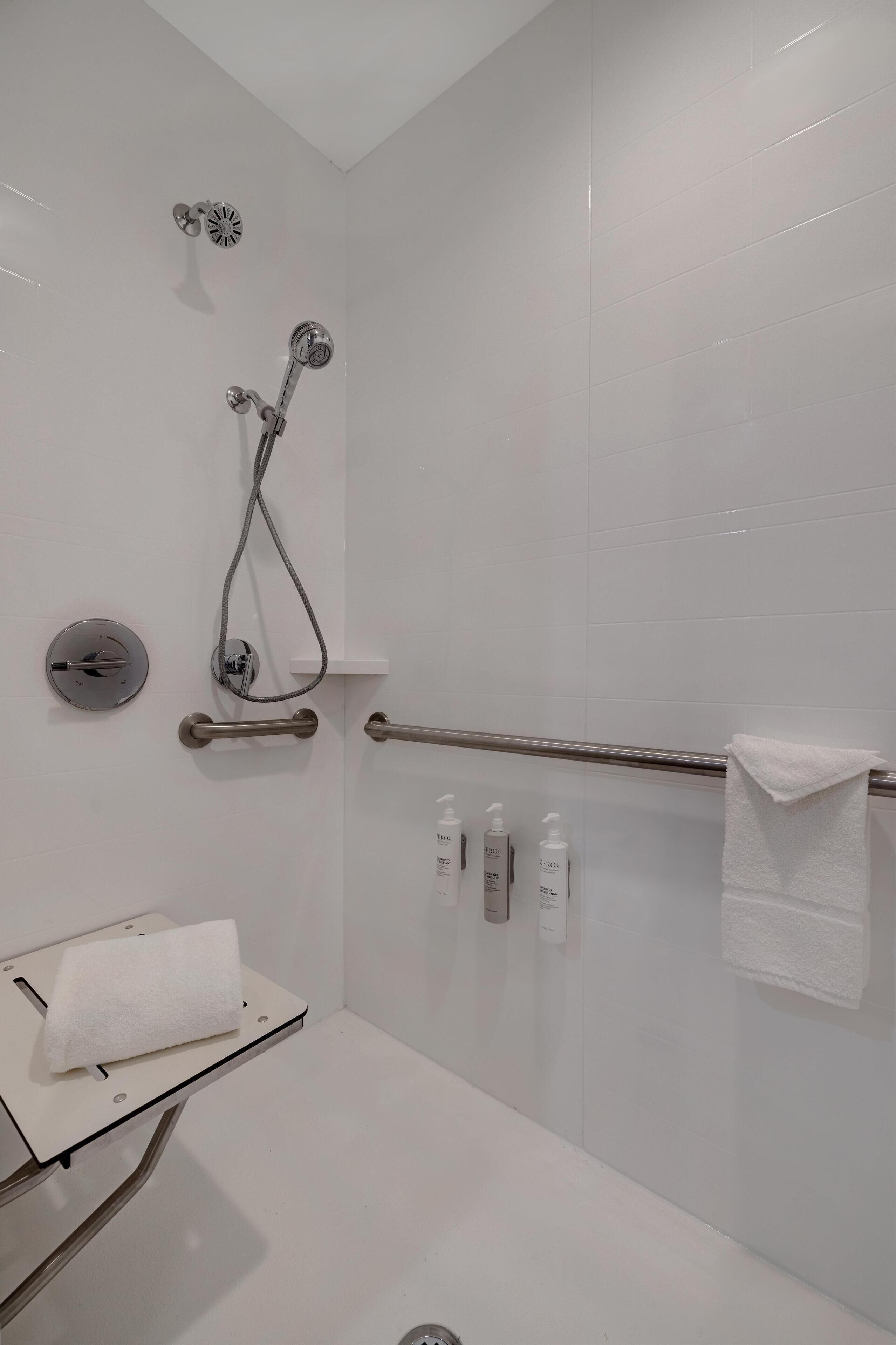 A modern bathroom with a glass shower enclosure, a handrail, a towel rack, and toiletries.