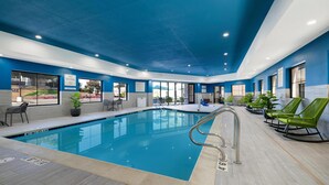 An indoor swimming pool with a blue ceiling, seating area with chairs, and a view of the outside. - Hampton Inn & Suites Marina (Marina)