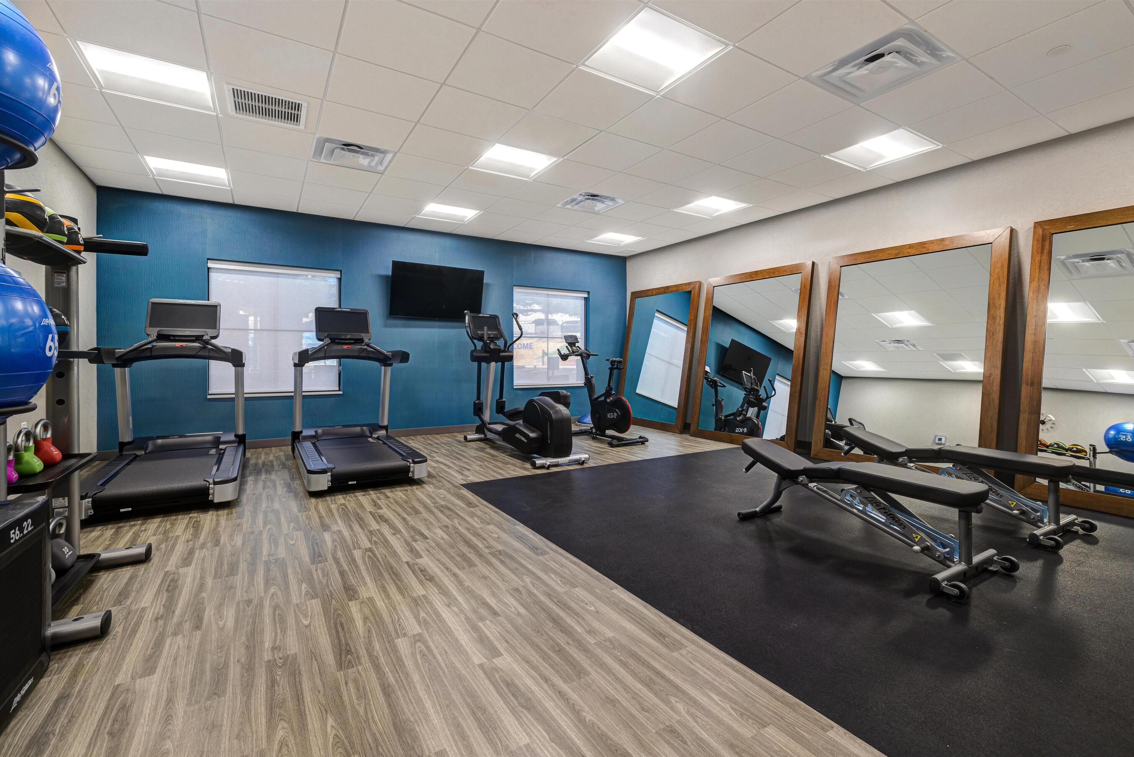 A gym with treadmills, exercise bikes, and a bench press.