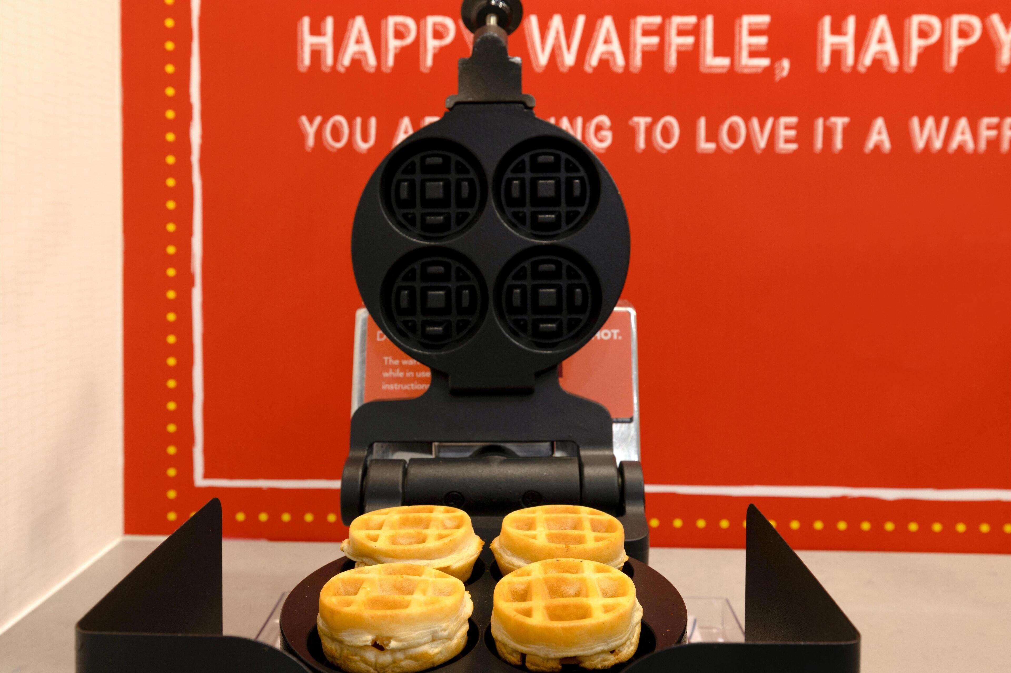 A waffle maker with four waffles on a plate, set against a red background with text.