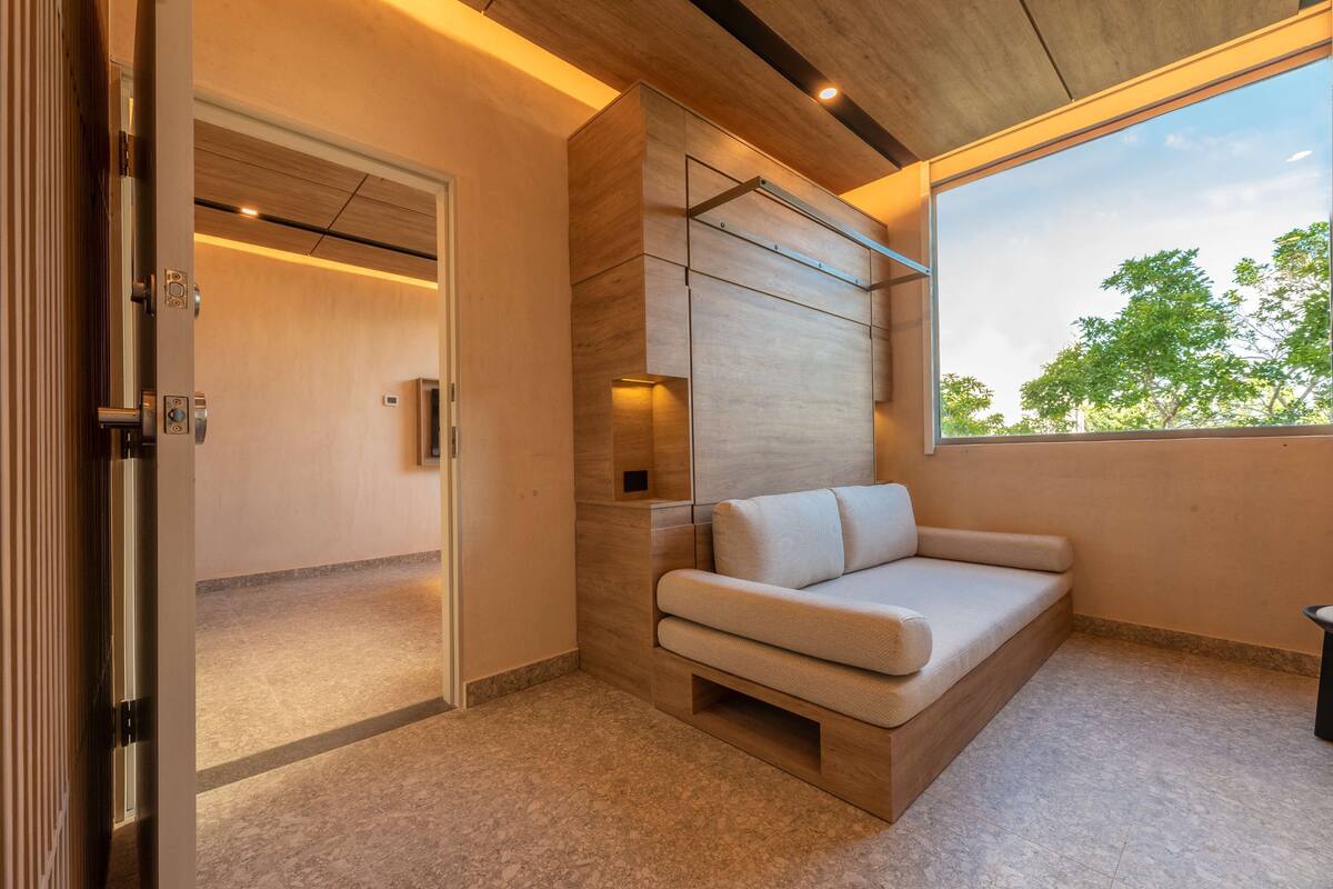 A modern interior with a built-in sofa, a wooden accent wall, and a large window offering a view of trees.