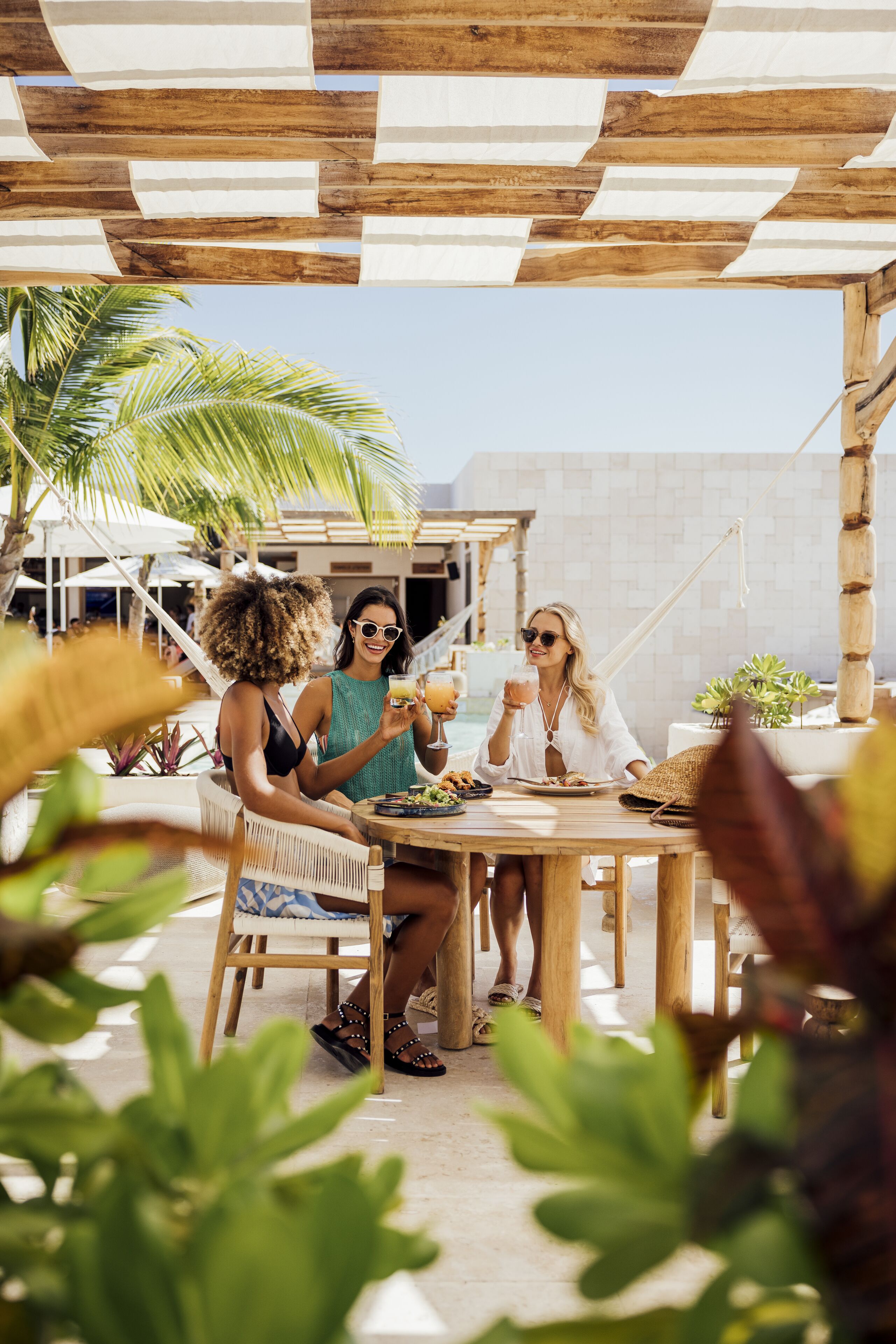A wooden outdoor seating area with a table, chairs, and a palm tree in the background.