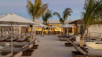 Un resort con varias zonas de descanso, palmeras y un edificio con un bar al fondo.