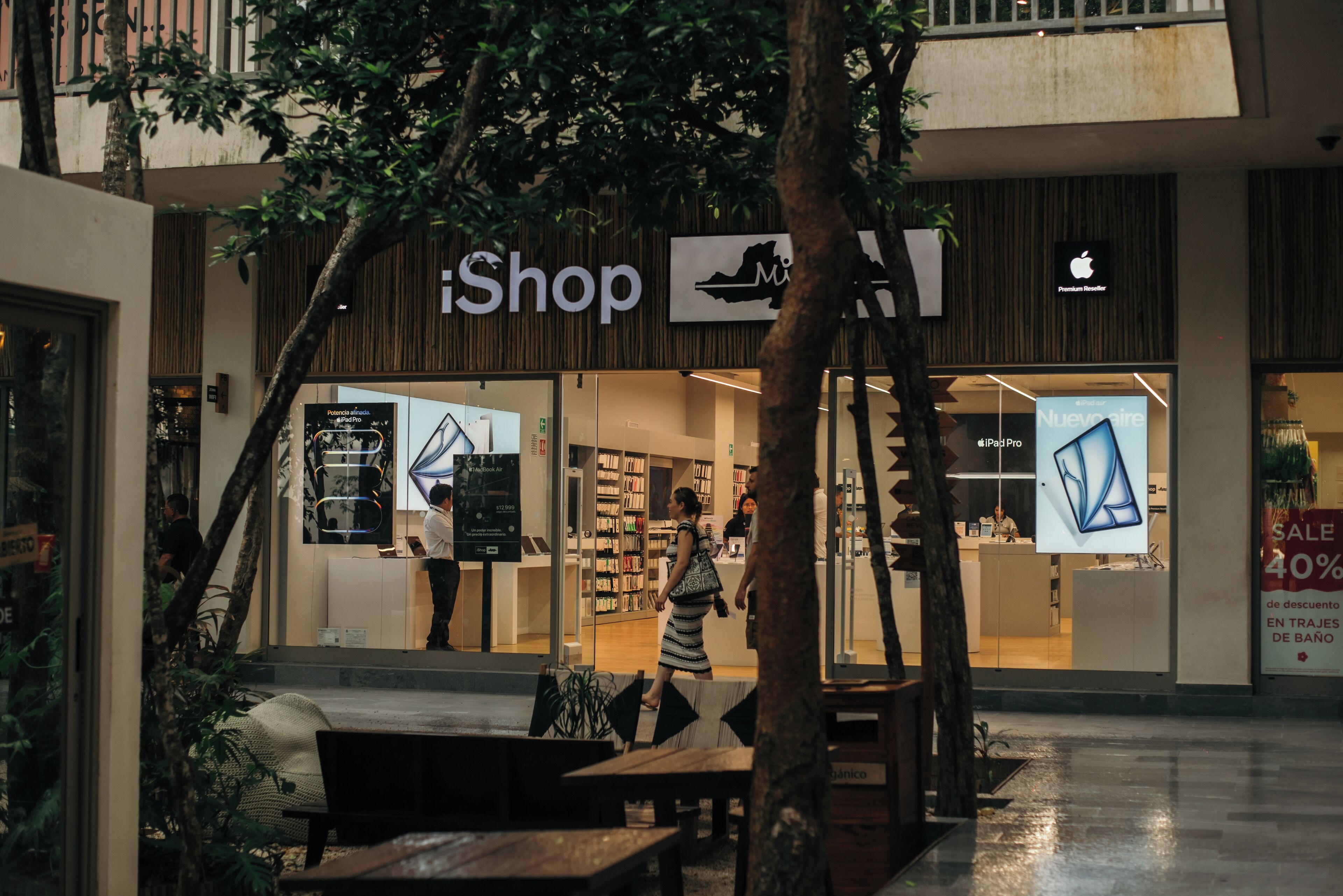 An iShop store with a modern interior, a visible staircase, and a seating area outside.