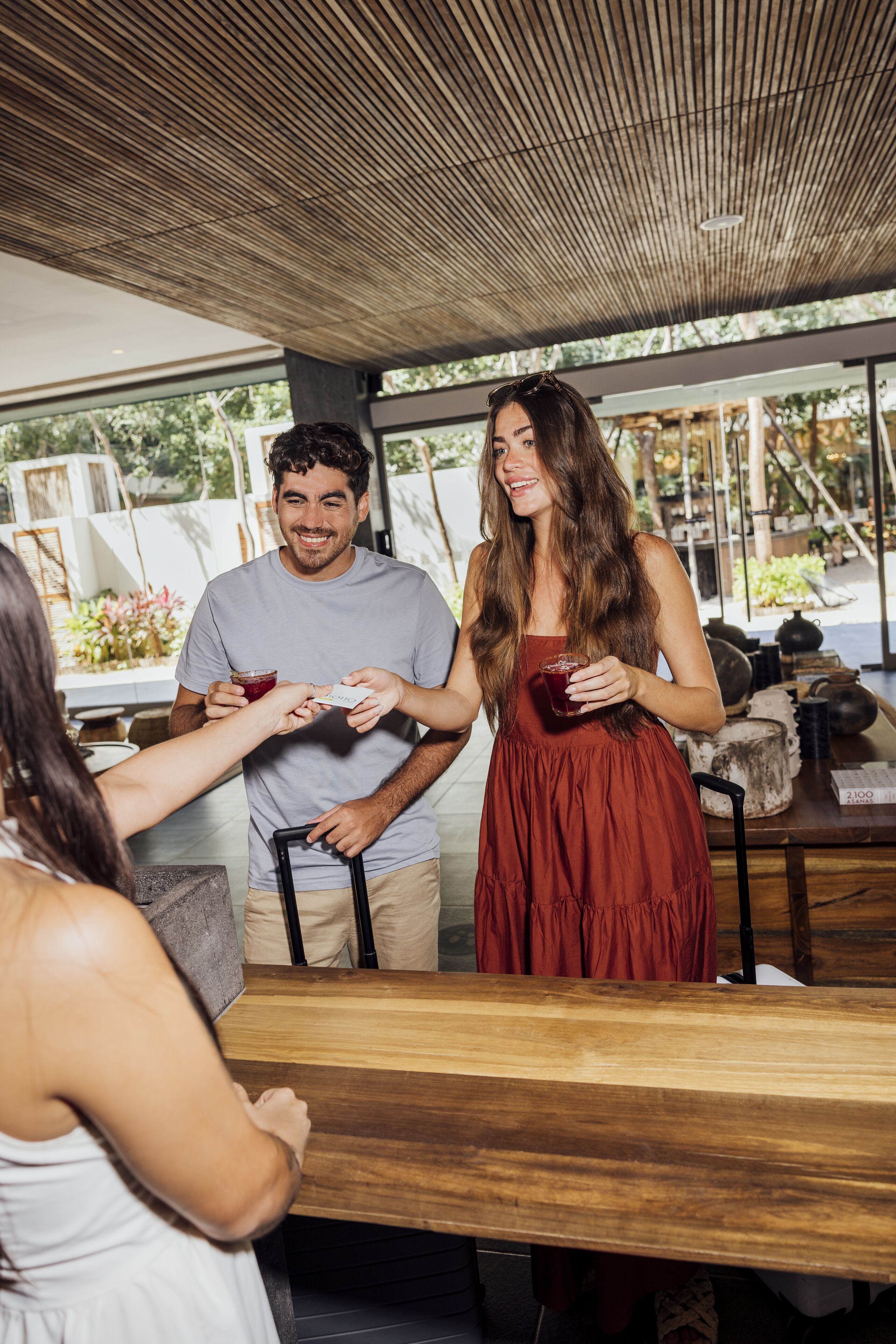 A wooden table with a menu, a person holding a drink, and another person handing over a card.