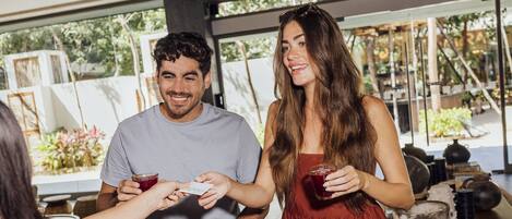 A wooden table with a menu, a person holding a drink, and another person handing over a card.