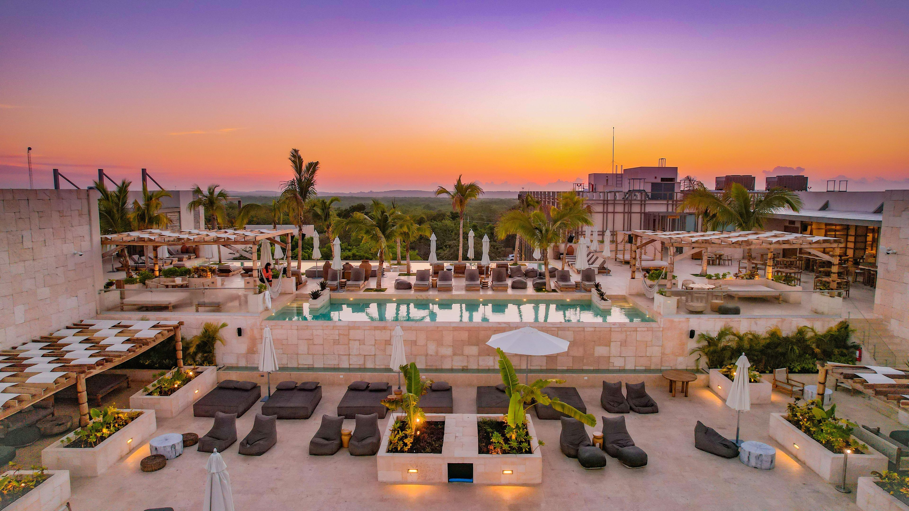 A rooftop pool area with lounge chairs, umbrellas, and a view of the sunset.